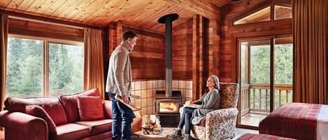 A cozy cabin interior with a wooden interior, a fireplace, a sofa, and a chair.