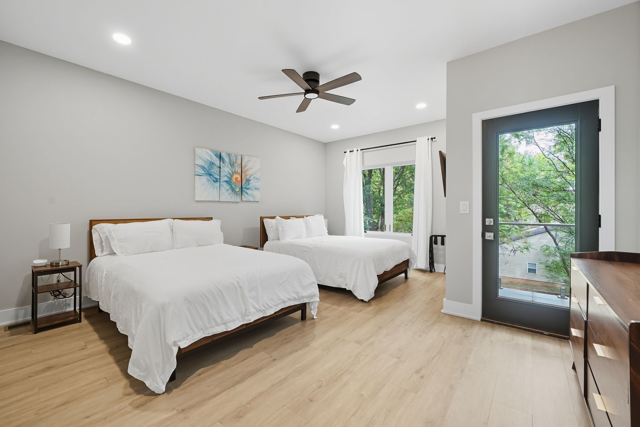 Une chambre avec deux lits, un ventilateur de plafond, une fenêtre avec des rideaux et une vue sur la verdure.