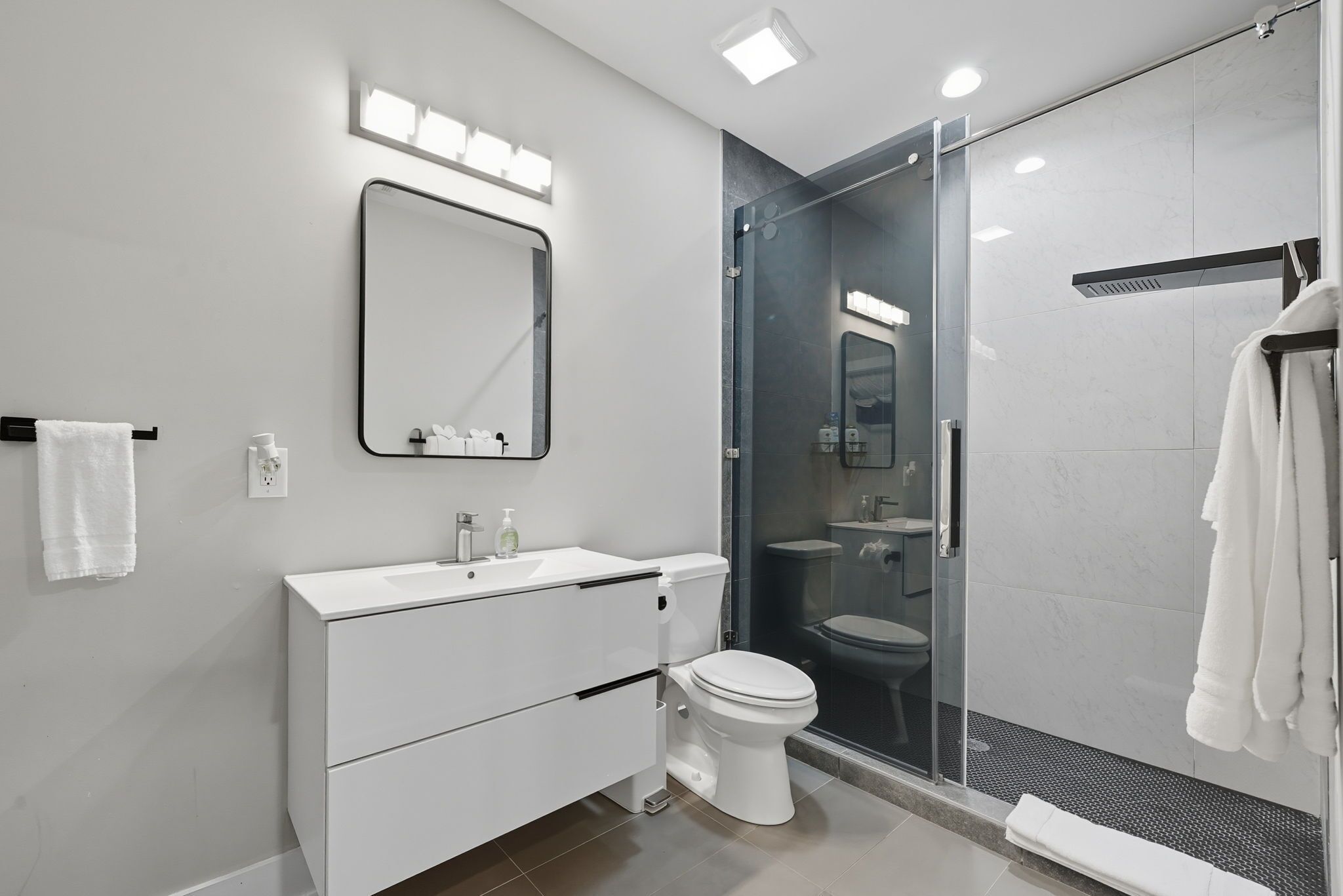 A modern bathroom with a white vanity, a glass shower enclosure, and a large mirror.