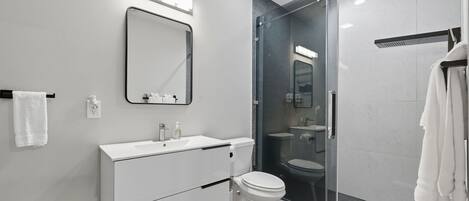 A modern bathroom with a white vanity, a glass shower enclosure, and a large mirror.