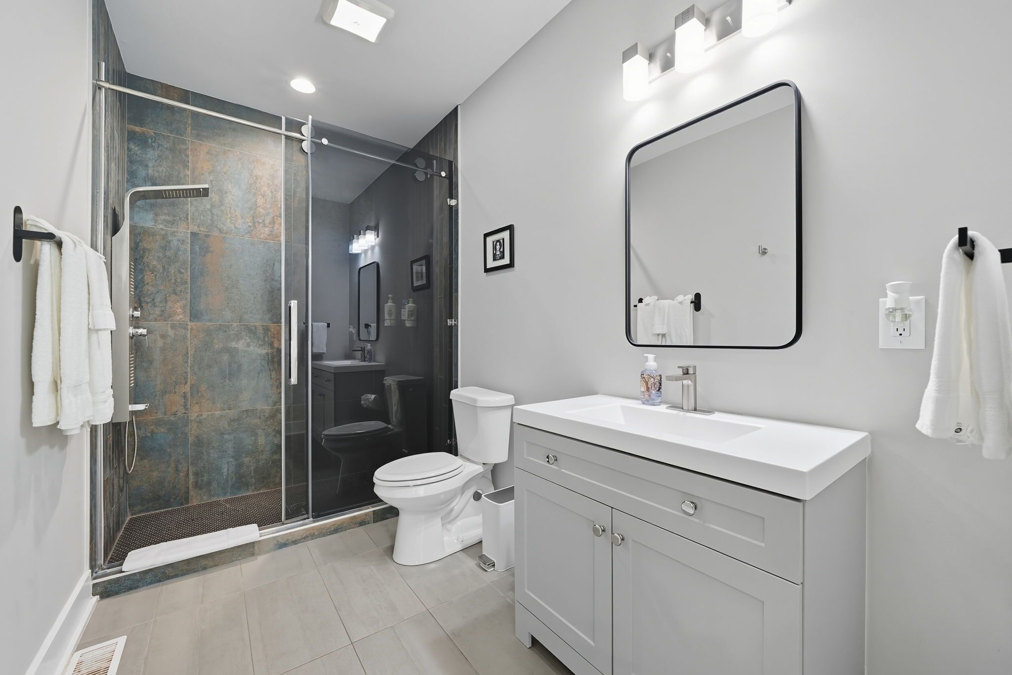 Une salle de bain moderne avec une douche à l’italienne en verre, un lavabo blanc et un grand miroir.
