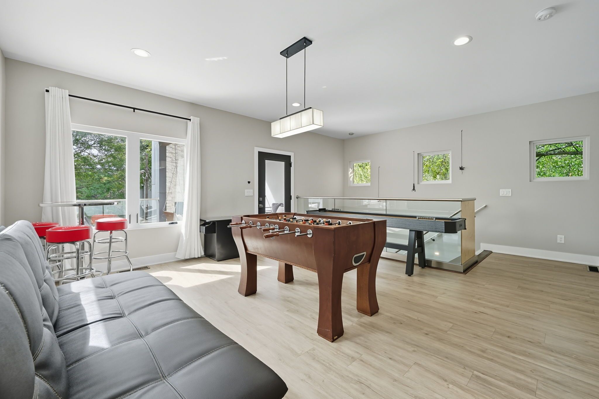Una sala de estar moderna con mesa de futbolín, un sofá gris y una zona de bar con taburetes.