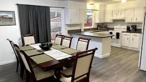 Un comedor con mesa y sillas de madera, una cocina con armarios blancos y un suelo gris.