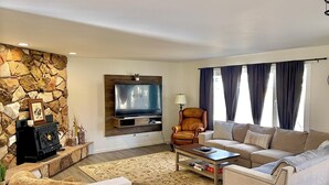 Una sala de estar con pared de piedra, televisión, chimenea, sofá, mesa de centro y ventana con cortinas.