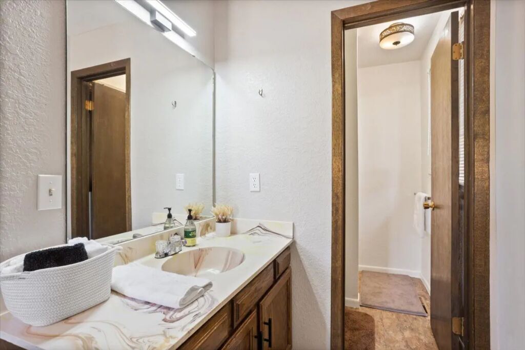 A bathroom with a double sink, a large mirror, and a wooden door leading to a shower area.