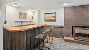 Eine Barbereich mit Holztresen, zwei Barhocker, einem Kamin aus Ziegelsteinen und zwei gerahmten Bildern an der Wand.