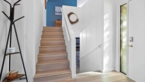 Eine Treppe mit Holzbodenstufen führt zu einer Zwischenebene, an Wänden sind weiße Wände und eine Tür mit Fensterglas zu sehen.