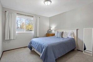 Une chambre à coucher avec un lit, une table de chevet, une lampe et une fenêtre avec des rideaux.