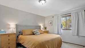 Ein Schlafzimmer mit Bett, Nachttischen, einem Fenster mit Vorhängen und einer Deckenleuchte.