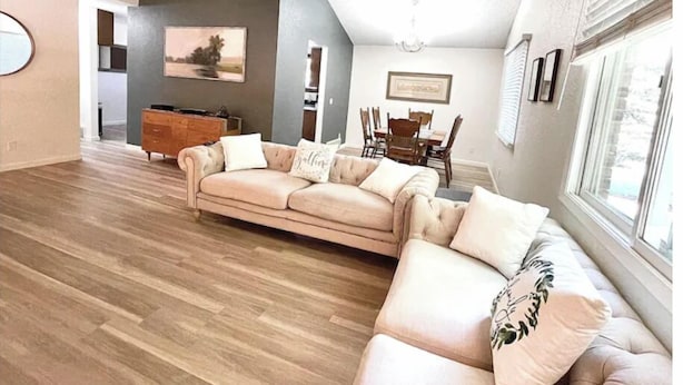 Ein geräumiges Wohnzimmer mit einem beigefarbenen Ecksofa, Holzboden und einem Essbereich mit Tisch und Stühlen.