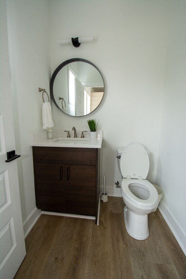 A bathroom with a white sink, dark wooden cabinet, a round mirror, and a white toilet.