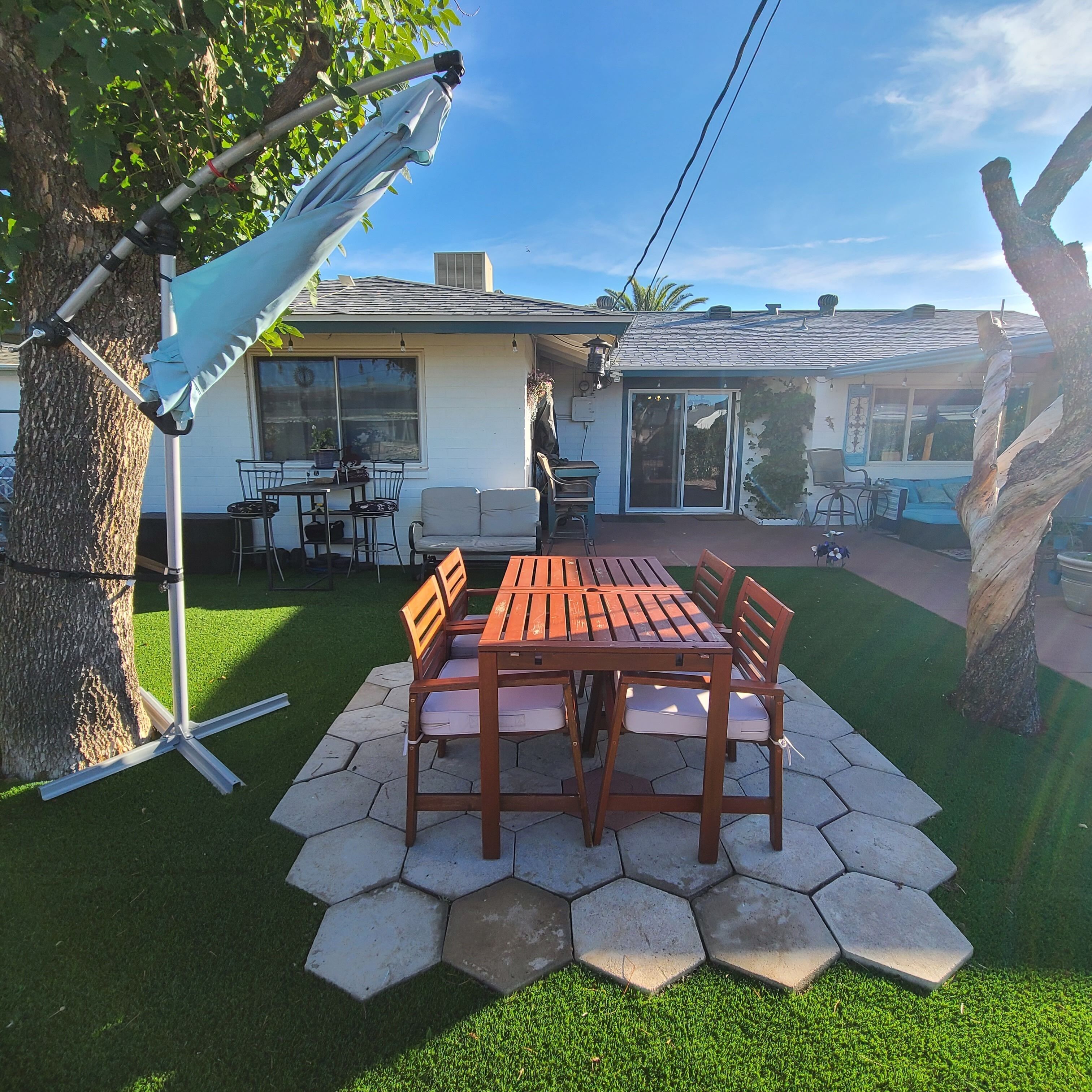 Een terras met een houten tafel en stoelen, omringd door honingraatvormige tegels en kunstgras.