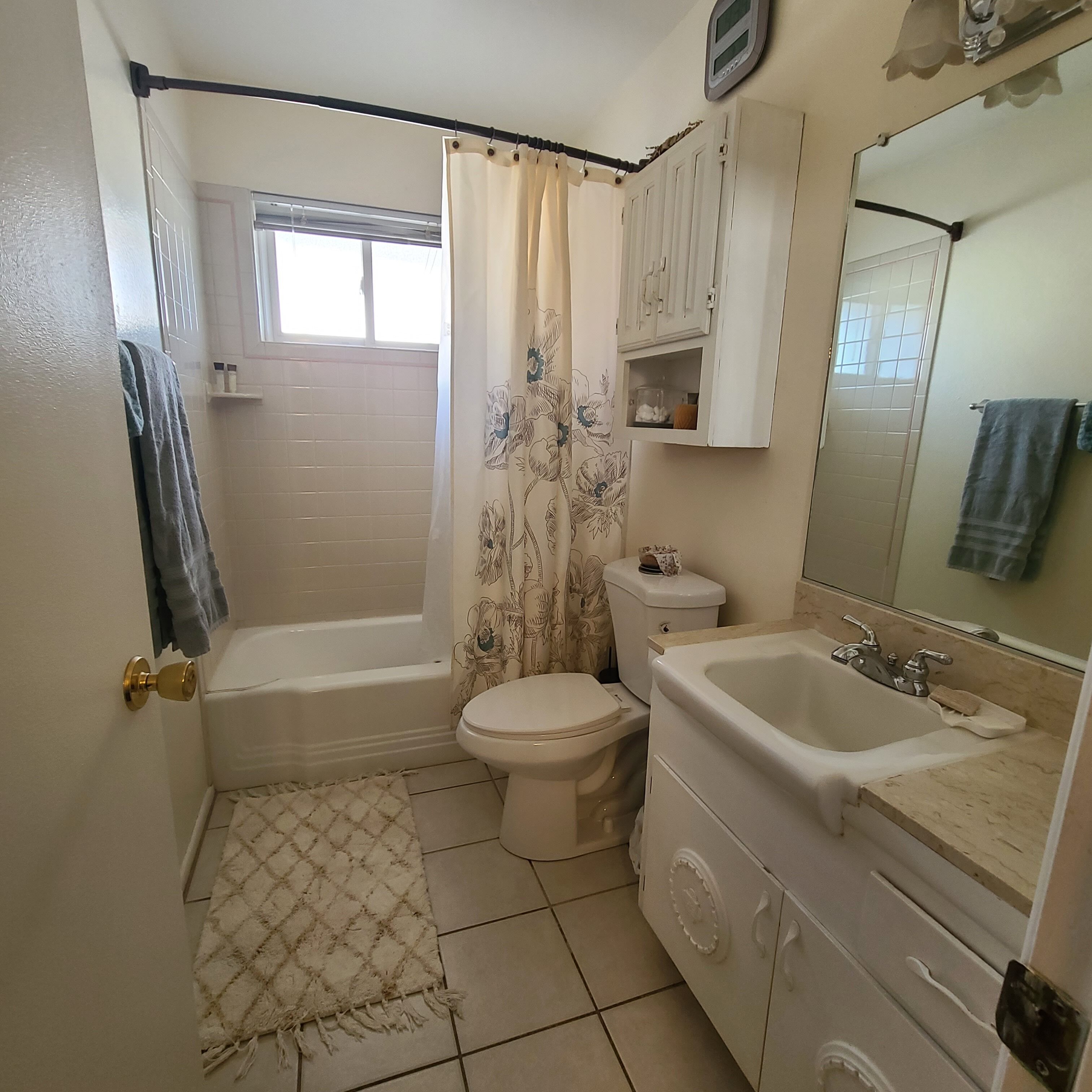 Ein Badezimmer mit Badewanne, Toilette, Waschbecken und einem Fenster mit Vorhang.