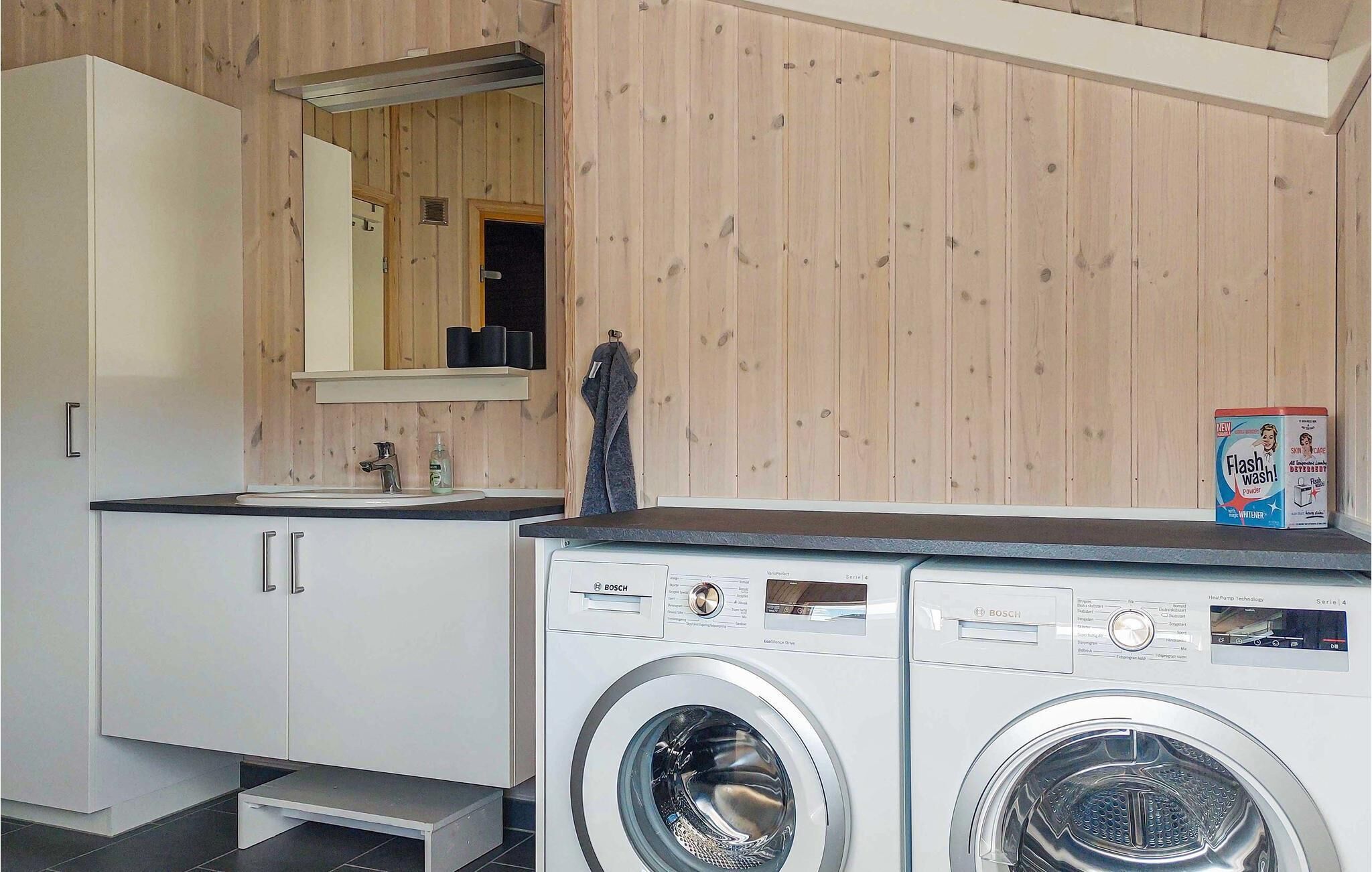 A modern laundry room with two Bosch washing machines, a sink, and a mirror above the counter.