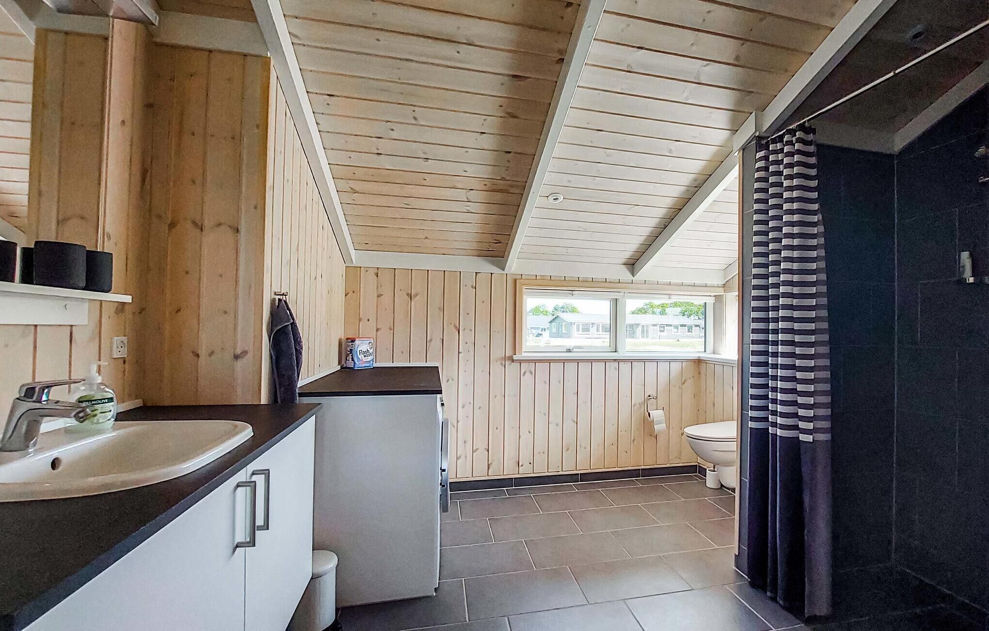 Une petite salle de bain avec un plafond en bois, un lavabo, des toilettes et une fenêtre qui laisse entrer la lumière naturelle.