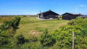 Un bâtiment noir doté d’un patio et d’une structure adjacente plus petite, le tout entouré d’une pelouse et d’un jardin bien entretenus.