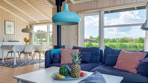 Un salon moderne comprenant un canapé, une table à manger et une grande fenêtre donnant sur un paysage verdoyant.