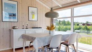 Une cuisine moderne avec des meubles blancs, une table à manger avec des chaises et une grande fenêtre donnant sur un paysage verdoyant et un immeuble.
