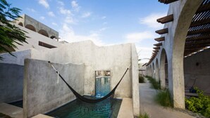 Una hamaca sobre una piscina con vistas a un edificio con arcos y un cielo despejado.