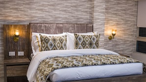 Une chambre moderne avec un cadre de lit en bois, une literie à motifs et des luminaires fixés au mur.