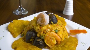 Une assiette de fruits de mer comprenant des crevettes, des moules et du riz, accompagnée d’un verre de vin rouge et d’un salier, le tout posé sur une table en bois.