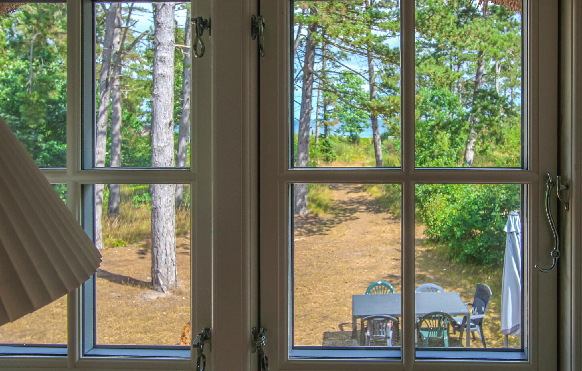 Ein Fenster mit Blick auf eine bewaldete Landschaft und ein Tisch mit Stühlen davor.