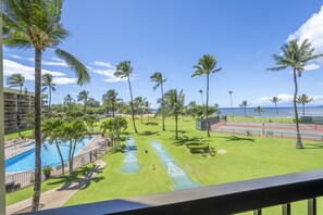 A pool area with palm trees, a tennis court, and a view of the ocean. - Oceanfront 2 bedroom suite in Sunny Kihei (Kihei)