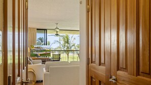Ein Zimmer mit Balkon, Deckenventilator und Blick auf Palmen.
