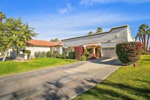 A two-story house with a red-tiled roof, a front porch, and a driveway leading to the garage. - Cozy Home in Palm Desert (Palm Desert)
