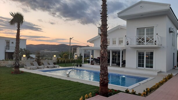 Una casa moderna de dos pisos con piscina, mobiliario exterior y vistas a las montañas.
