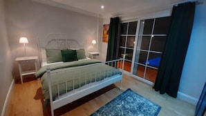Un dormitorio con cama, dos mesitas de noche, una ventana con cortinas y vistas al exterior.