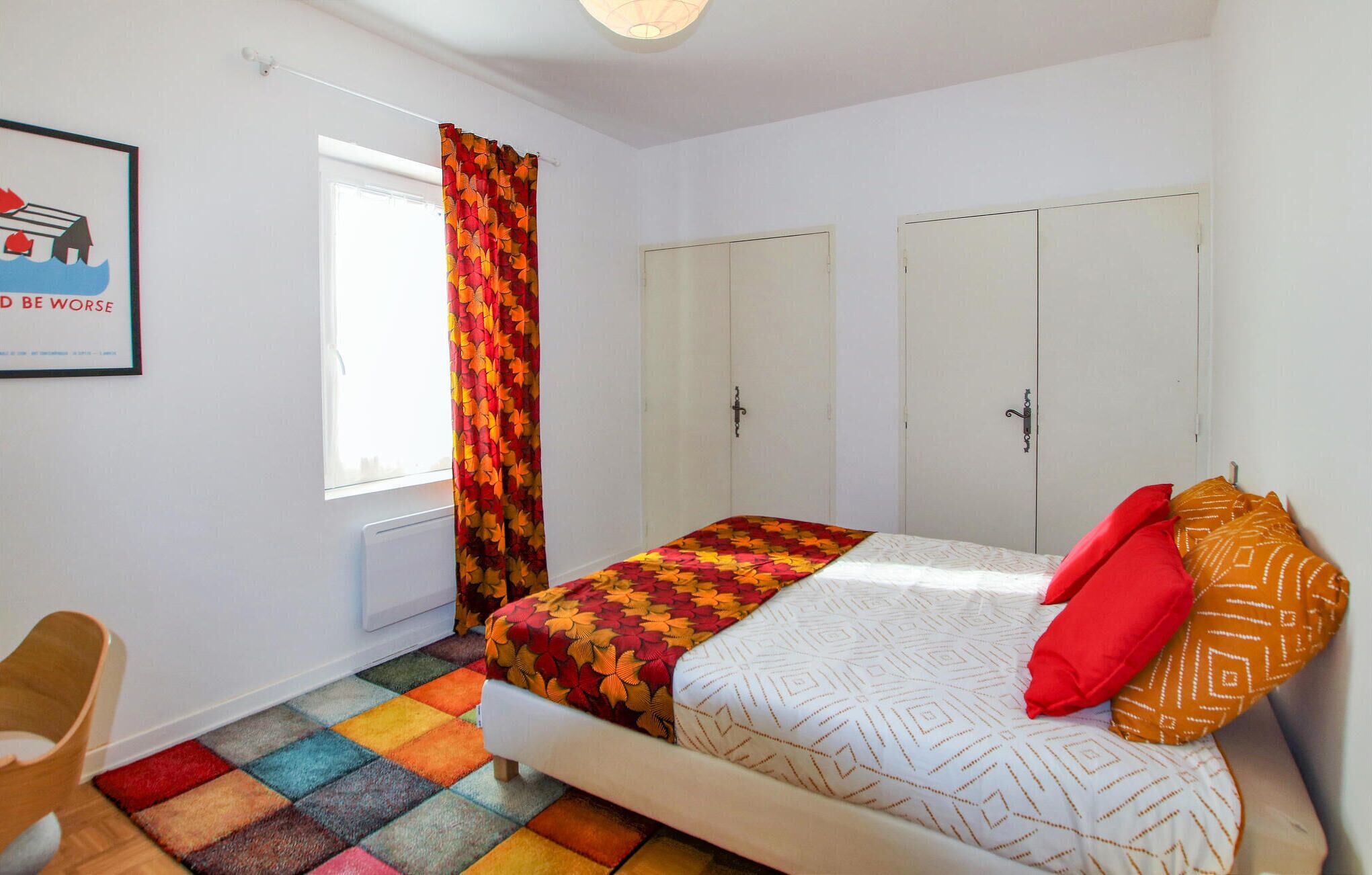 A bedroom with a bed, a window with curtains, a radiator, and a wardrobe.