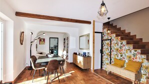 Een ruime woonkamer met een eettafel, stoelen, een bank en een trap met bloemenbehang.