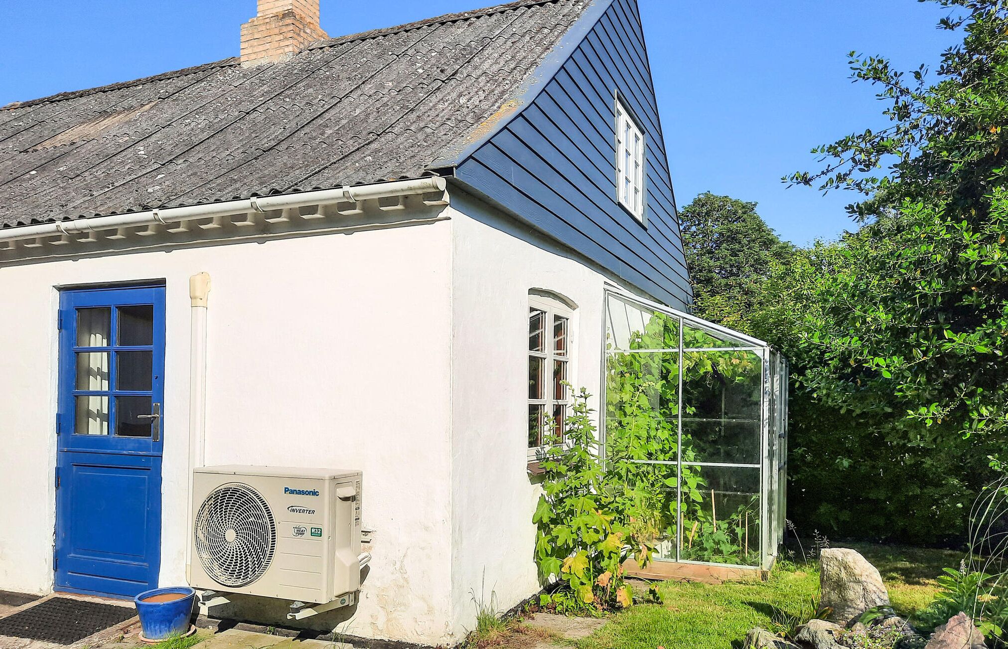 Une maison blanche avec une porte bleue et une serre en verre attenante sur le côté.