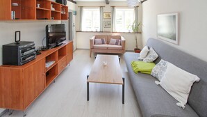 Una sala de estar con un mueble de entretenimiento de madera, un sofá gris, una mesa de centro de madera y una ventana con cortinas.