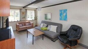 Una sala de estar con un sofá gris, un sillón de cuero negro, una mesa de centro de madera y un televisor sobre un mueble de madera.