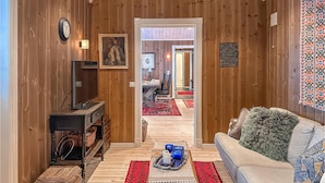Een gezellige kamer met houten inrichting, een bank, een televisie en een zithoek met een rood vloerkleed.