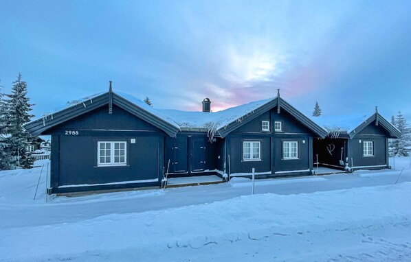 Une maison aux couleurs sombres, à plusieurs étages, avec le numéro « 2988 » inscrit sur la façade, et entourée de neige.