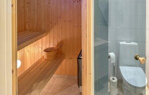 Un sauna avec des murs et un banc en bois, une cabine de douche en verre avec des toilettes, et un porte-serviettes.