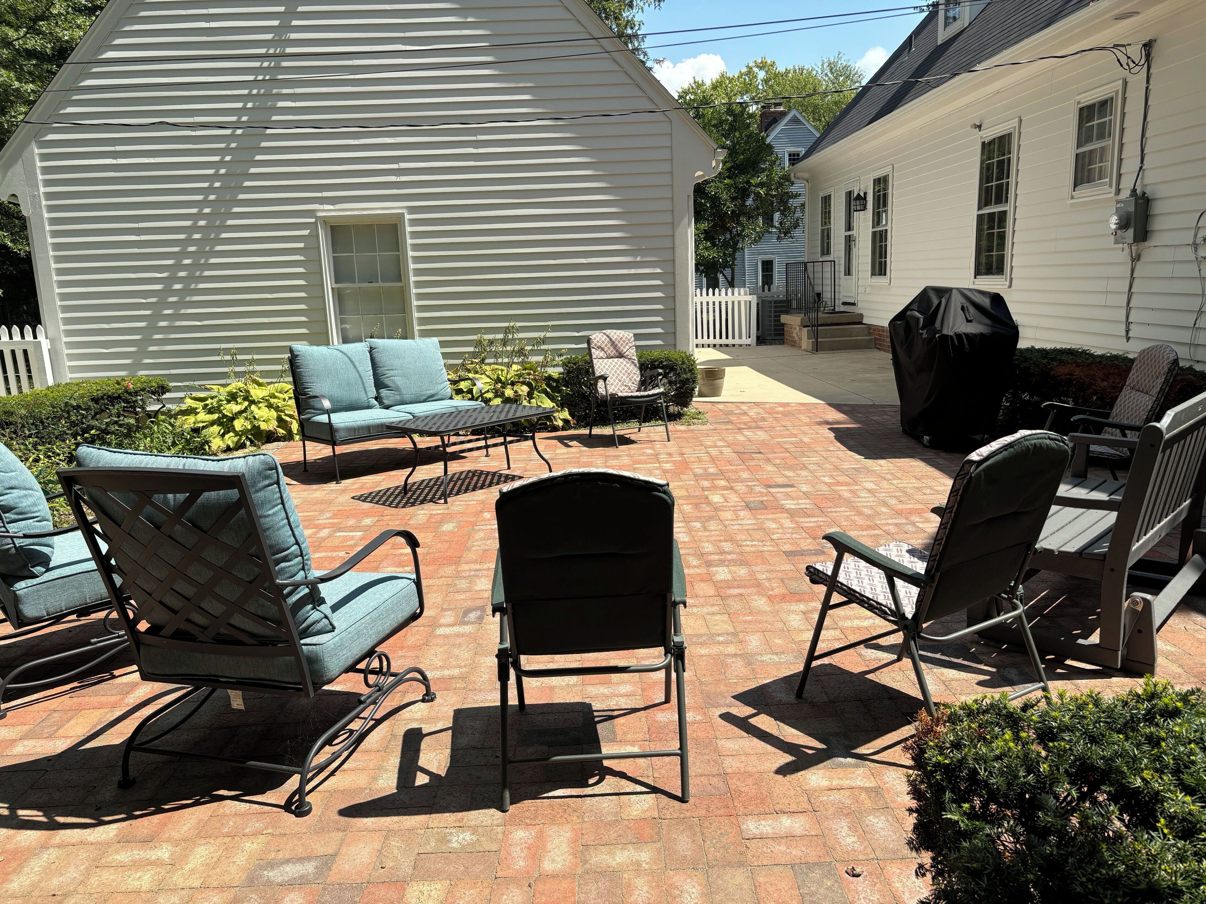 A patio with outdoor furniture, a grill, and a white house with a picket fence.