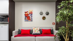 Una sala de estar moderna con un sofá gris, cojines rojo y gris, un cojín floral y un cuadro de flores rojas en la pared.