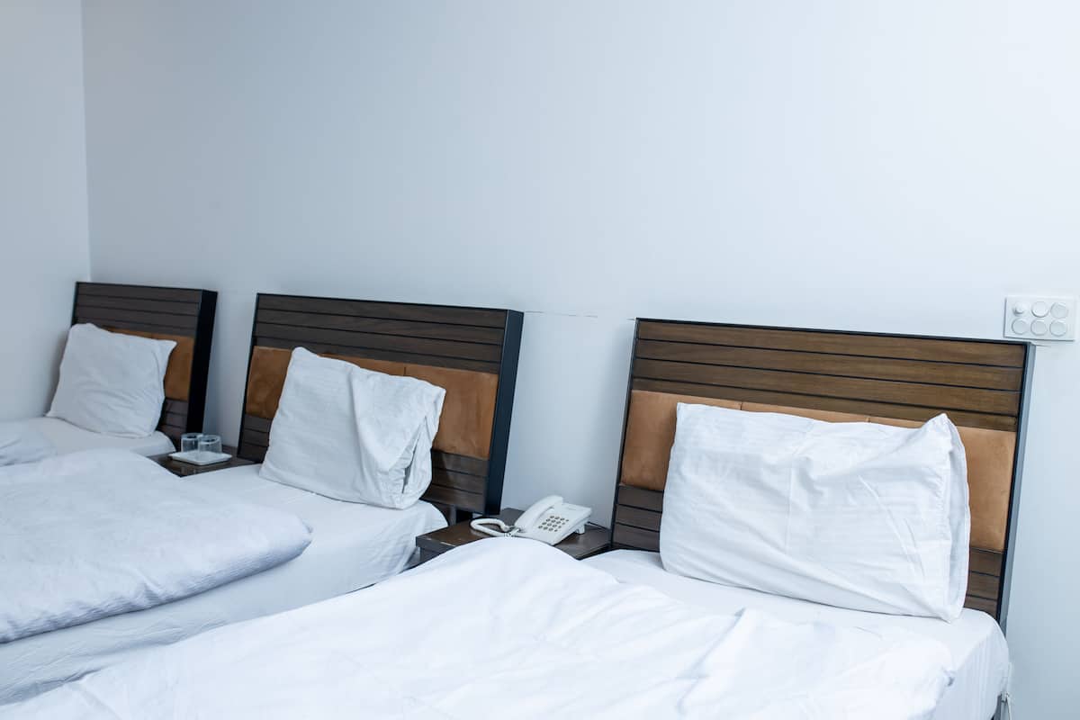 Une chambre d’hôtel avec deux lits, chacun doté d’une tête de lit en bois et de linge de lit blanc. On y trouve une table de chevet avec un téléphone blanc et un verre d’eau.
