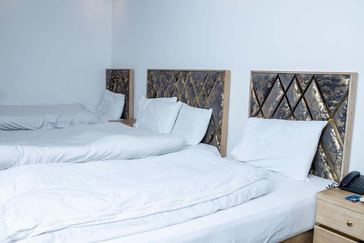 Une chambre d’hôtel avec trois lits, chacun doté de draps blancs et d’une tête de lit en bois. On y trouve une table de chevet sur laquelle sont posés un téléphone et un porte-clés.