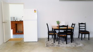 Kompakti keittiö, jossa on valkoinen jääkaappi, mikroaaltouuni ja puinen kaappi. Keitti össä on ruokapöytä, jossa on neljä tuolia, sekä pieni matto.