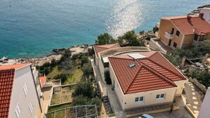 A coastal property with a terraced roof, a view of the sea, and a garden area.