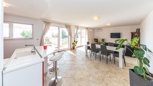 A spacious living area with a dining table, chairs, a TV, and a balcony with curtains.