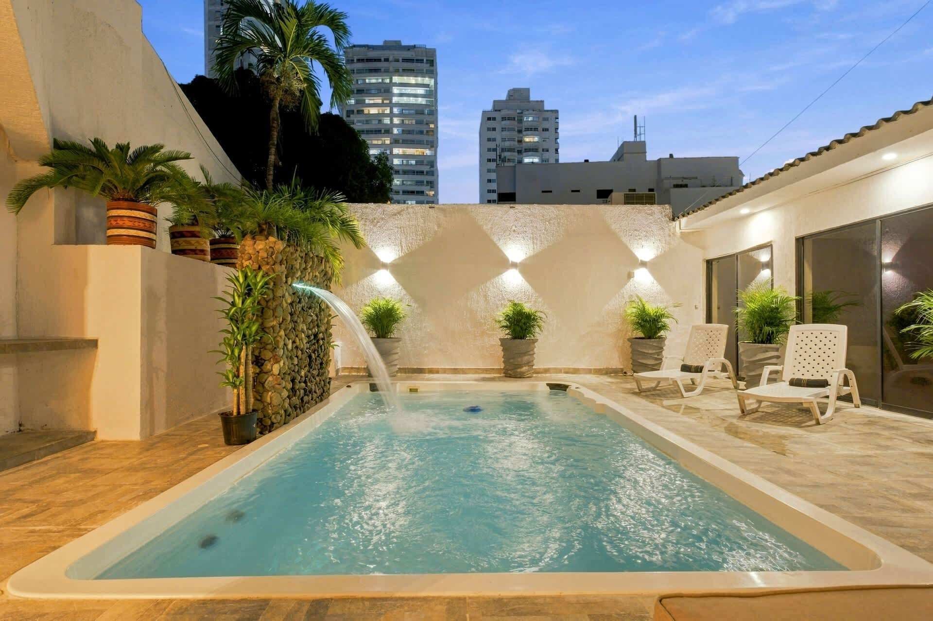 A swimming pool with a waterfall feature, surrounded by potted plants and lounge chairs.