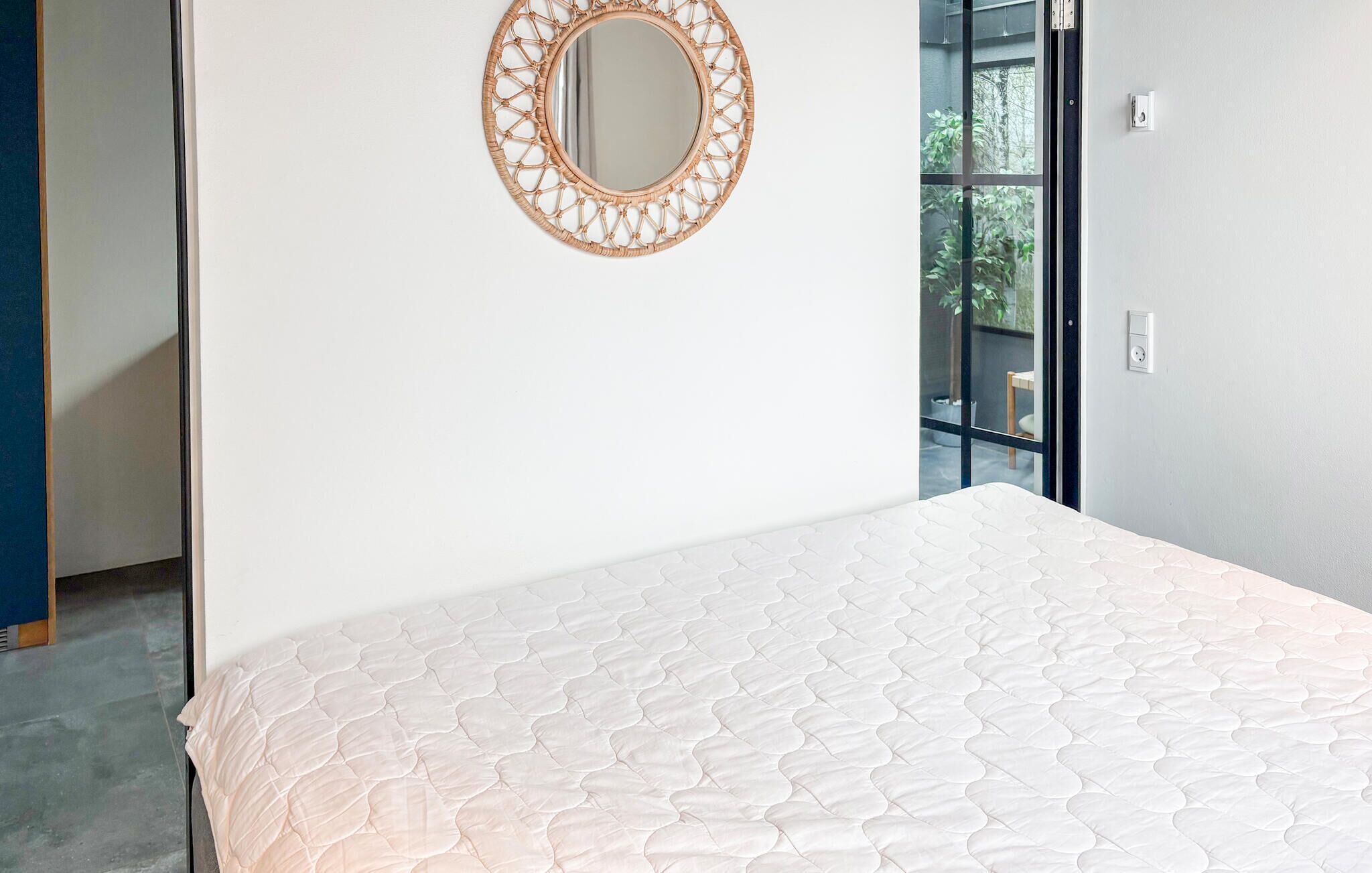 Ein Schlafzimmer mit einem Bett, einem runden Spiegel und einem Fenster mit Blick auf Grünflächen.