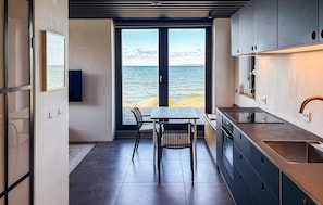 A modern kitchen with a view of the sea, a dining area with chairs, and a large window.