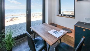 Ett rum med ett träbord, två stolar, ett litet skåp och utsikt över stranden.